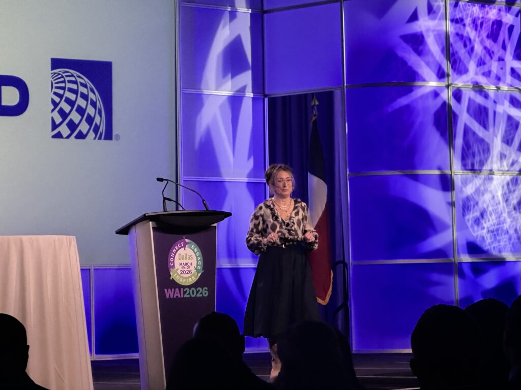A brunette woman with her hair pulled back and glasses standing next to a podium with the United Airlines logo in the background.