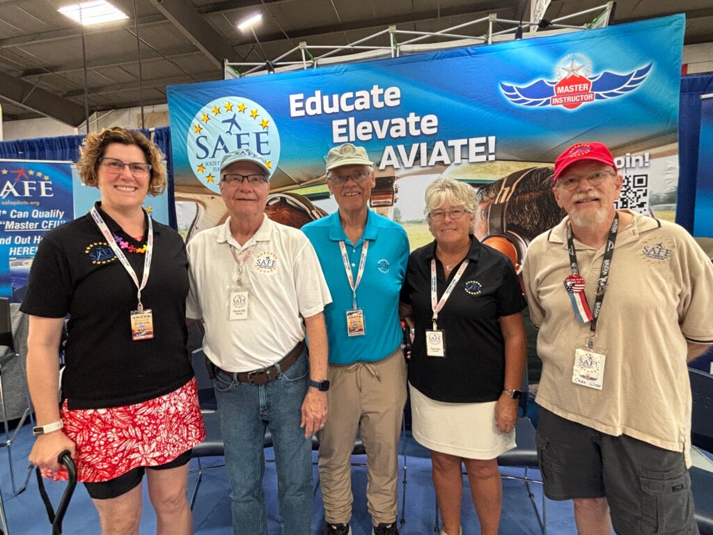 five people in polo shirts stand in front of a banner that says SAFE, Educate, Elevate, Aviate.