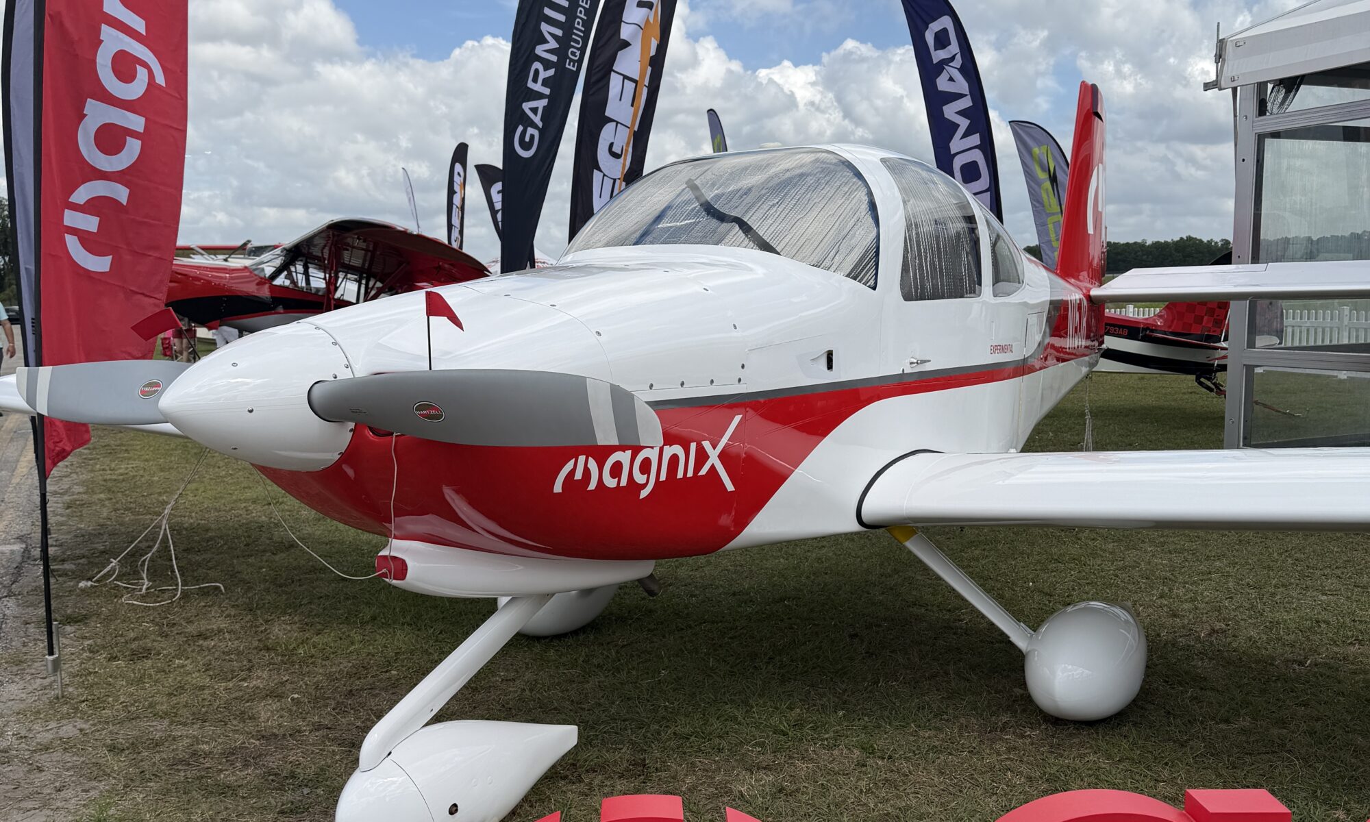 a van's RV-10 painted red and white with Magnix on the cowl and flags around it