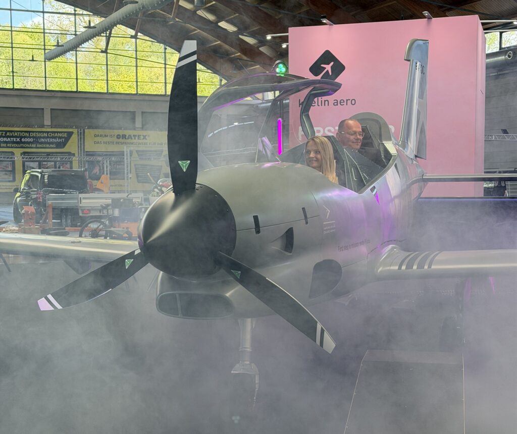 a gray tandem two seat airplane with a woman in front and a man in back shines out of fake fog