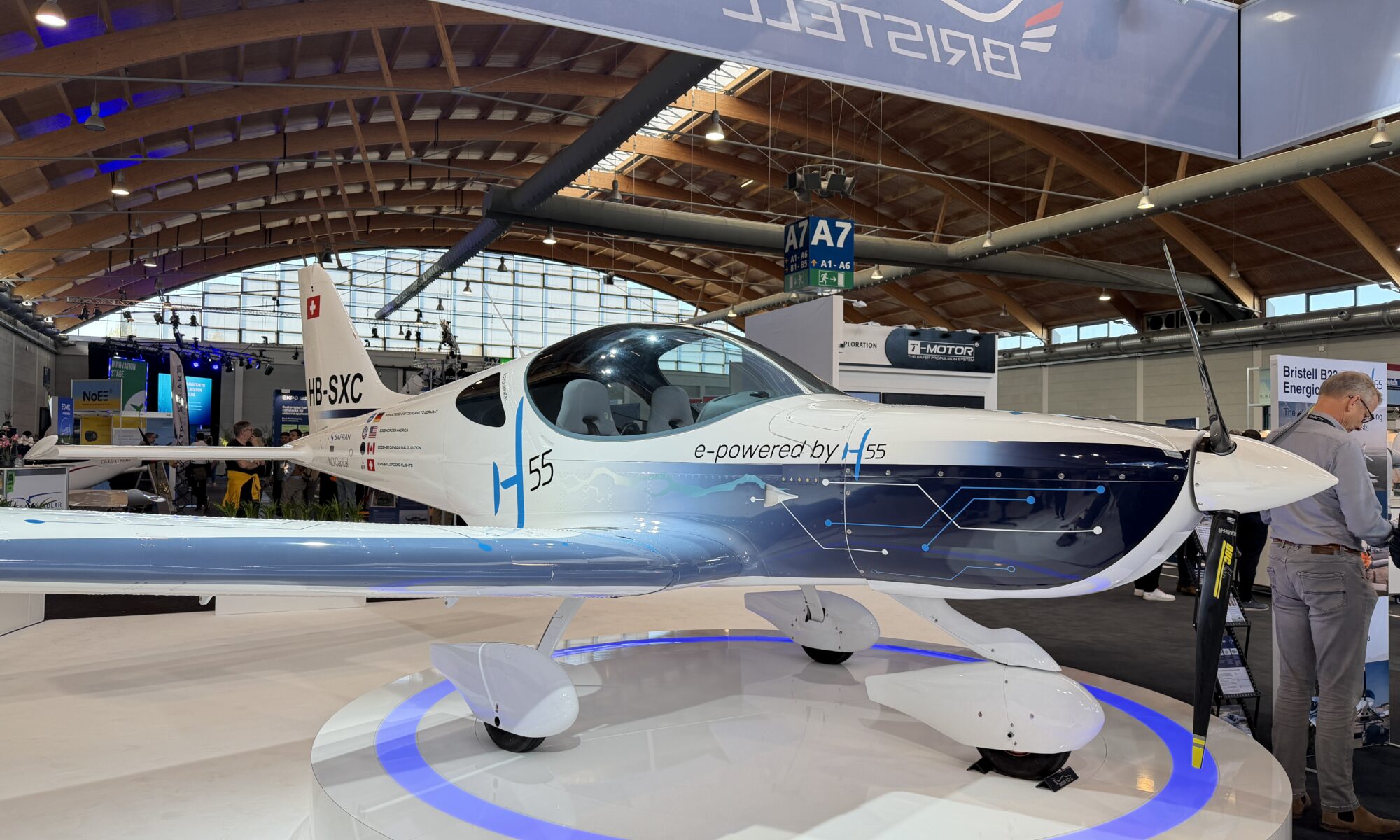 a white airplane with a digital gray and blue graphic on the cowl on a white platform